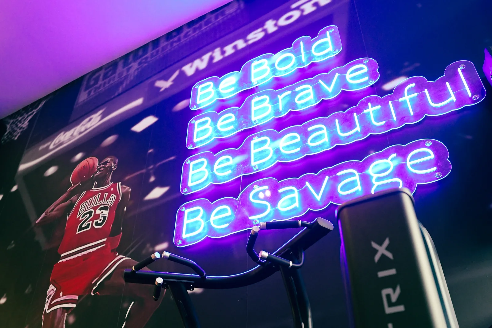 Be Bold, Be Brave, Be Beautiful, Be Savage neon manifesto wall above the training floor
