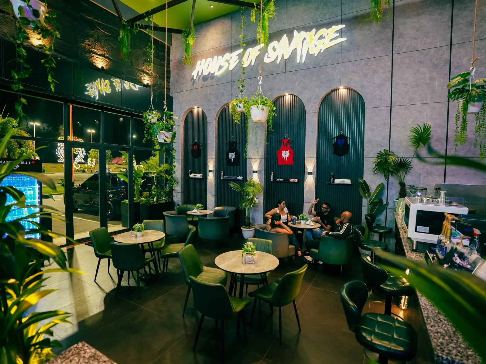 House of Savage café seating with green leather chairs, hanging plants and the Savage apparel wall