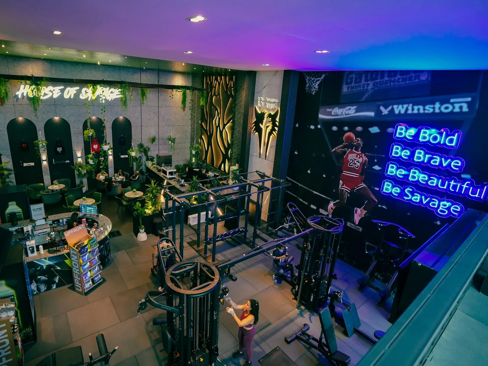 Overview of the Savage Elite Fitness atrium with the Be Bold, Be Brave, Be Beautiful, Be Savage neon wall above the training rig