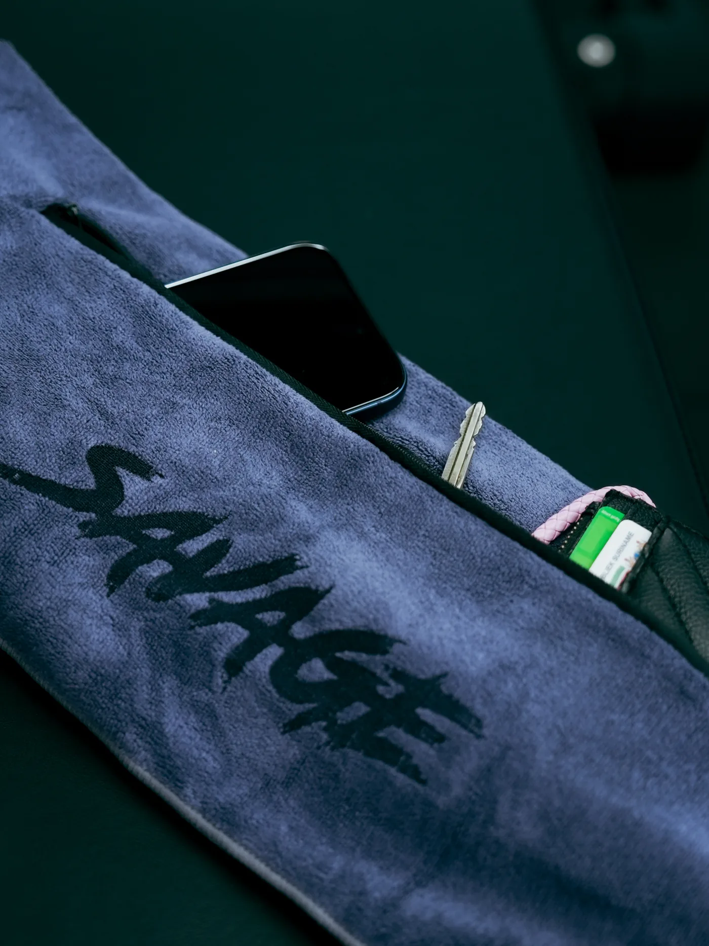 Branded Savage Elite Fitness towel with a phone and personal training essentials laid out on a dark bench.